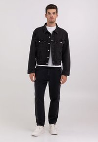 Sort denimjakke med vendt krave, forlommer og sølvknaplukninger, båret over en hvid t-shirt og parret med sorte bukser og hvide sneakers.