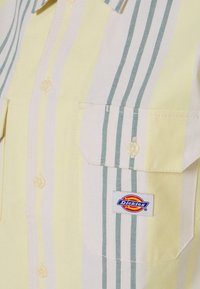 Rövid ujjú sárga és fehér ing zöld csíkokkal. Két mellzsebbe és Dickies logós címkével rendelkezik. Pamut anyagból készült.