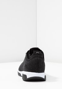 Schwarze Sport sneakers mit einem strukturierten Strick-Obermaterial, verstärktem Fersenbereich, weißer Mittelsohle und Gummiaußensohle. Keine sichtbaren Muster oder Marken.