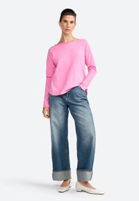 Maglietta rosa a maniche lunghe con una vestibilità rilassata, abbinata a jeans in denim a gamba larga con risvolto e scarpe bianche a tacco basso. Design semplice con dettagli discreti.
