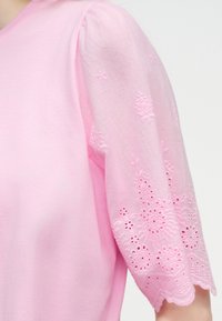 Ανοιχτό ροζ μπλουζάκι με φουσκωτά κοντά μανίκια που διαθέτουν περίπλοκη κεντημένη λουλουδένια διακόσμηση και μοτίβα με οπές.