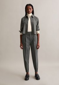 Grijze button-up shirt met lange mouwen, gelaagd over een crèmekleurige turtleneck. Gecombineerd met grijs gestreepte broeken en stevige zwarte loafers.