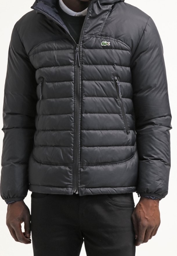 Doudoune noire avec fermeture éclair à l'avant et poches latérales zippées, portée par une personne les mains détendues le long du corps.