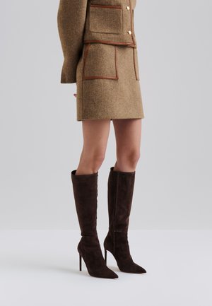 Brun tweed blazer- og skjørtsett med kontrastkant, kombinert med mørkebrune semsket skinn knelengde stiletthæler. Teksturdetaljer er synlige i stoffet.