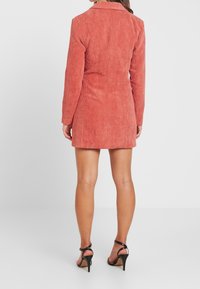 Světlá korálová kordurová bunda, módně střižená, s dlouhými rukávy a límečkem, s vertikálními jemnými pruhy a přiléhavým střihem.