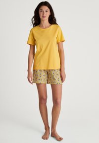 Gele katoenen t-shirt met korte mouwen, gecombineerd met een patroon short in een gele, witte en marineblauwe bloemdesign.