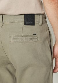 Pantaloni khaki realizzati in denim testurizzato con un'etichetta nera che riporta la scritta "ONLY & SONS." Presentano una tasca laterale e dettagli cuciti.