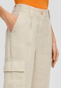 Beige linnen cargo broek met zijzakken, geplooid ontwerp en een enkele knoopsluiting bij de taille. Lichtgewicht textuur, casual stijl.