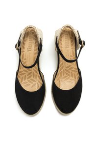 Sandales à talons compensés en suède noir avec un talon tressé beige, bout rond, bride ajustable à la cheville, et semelle en cuir à motifs avec un design de feuilles.
