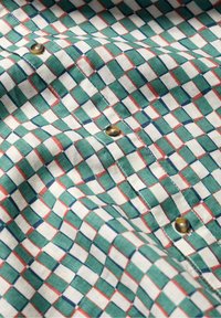 Camisa estampada con un diseño de cuadrícula en verde, blanco, rojo y azul, hecha de una tela de textura suave y con botones de latón.
