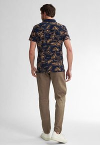 Maglietta a maniche corte blu navy con un motivo floreale nei toni dell'oro, abbinata a pantaloni marrone chiaro e sneakers bianche, che mostrano un look casual.