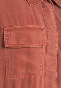 Roodbruine shirt met een borstzak, gemaakt van gestructureerde stof met zichtbare stiksels en een klassiek kraagontwerp.