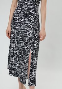 Vestido de patrón en blanco y negro con un corpiño ajustado, abertura lateral y una tela fluida. Presenta estampados abstractos y una textura suave.