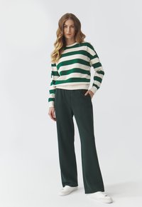 Pull à rayures vertes et blanches à manches longues, associé à un pantalon large vert foncé et des baskets blanches. Design simple et décontracté.