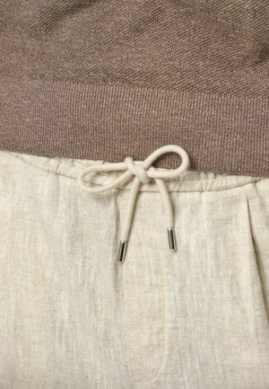 Bruine gebreide trui met geribde zoom, gecombineerd met lichtbeige linnen broeken met een trekkoord met zilveren metalen uiteinden.