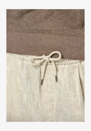 Bruine gebreide trui met geribde zoom, gecombineerd met lichtbeige linnen broeken met een trekkoord met zilveren metalen uiteinden.