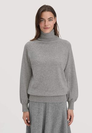 Grauer Strickpullover mit Rollkragen, Raglanärmeln und geripptem Saum. Weiche Textur und lässige Passform. Kombiniert mit einem passenden grauen Rock.