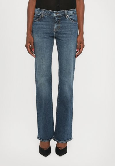 Blue denim flared jeans with a faded finish, five-pocket design, and stitching details. Worn with black high-heeled shoes.