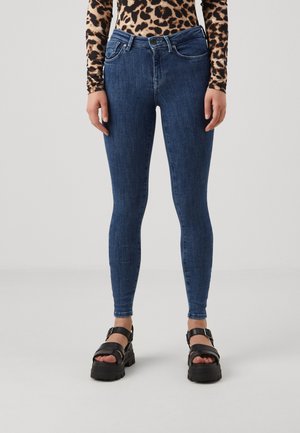 Jean bleu slim avec taille mi-haute, design à cinq poches et détails de couture subtils, associés à des sandales noires épaisses.