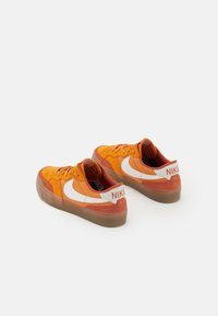 Sneaker in suede arancione e rosso con logo Nike bianco, suola in gomma e accentuazioni testurizzate. Presenta un collo imbottito e design con lacci.