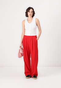 Top blanco de canalé sin mangas, pantalones rojos de tiro alto con pliegues, bolso rosa anudado y zapatillas negras con suelas ligeras.