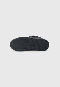 Black sneaker sole featuring textured rubber, prominent tread patterns, and a curved toe shape for improved grip and durability.