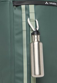 Bottiglia d'acqua in acciaio inossidabile attaccata a una borsa in tessuto verde con texture, strisce di accentuazione verde chiaro e una cerniera nera.