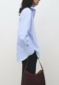 Camicia azzurro chiaro a maniche lunghe con colletto a punta, polsini con bottoni, abbinata a pantaloni neri e una borsa bordeaux. Design semplice e su misura.