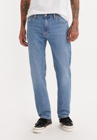Lyseblå denim jeans med rett ben, som har knappedlukking, sidelommer og subtile stingdetaljer. Brukt med svarte joggesko.