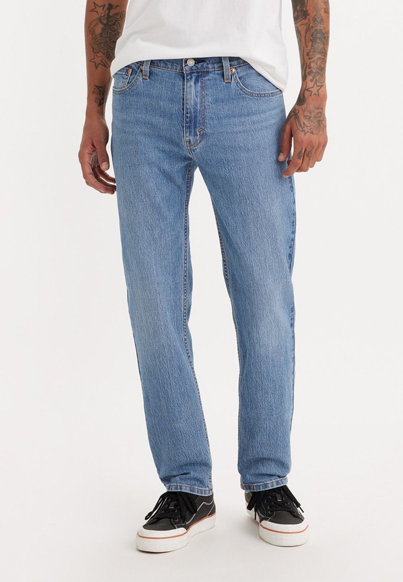 Lyseblå denim jeans med rett ben, som har knappedlukking, sidelommer og subtile stingdetaljer. Brukt med svarte joggesko.