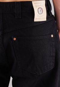 Schwarze Denim-Jeans mit einem Leder-Logoanhänger, ausgestattet mit Gesäßtaschen mit Kupfennieten und dezenten Stickdetails.