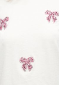 Τρία ροζ και ασημί λαμπερά αυτοκόλλητα σε σχήμα φιόγκου σε λευκό υφασμάτινο φόντο, τοποθετημένα κοντά στις άκρες και στο κέντρο.