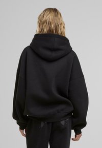 Schwarzer, übergroßer Hoodie mit hohem Kragen und großer Kapuze. Weicher Stoff mit abgesenkten Schultern und gerippten Bündchen. Einfaches, schnörkelloses Design.