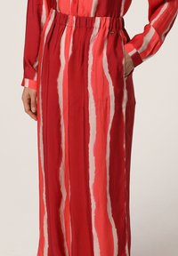 Gonna lunga a righe rosse e rosa con vita elasticizzata, indossata con una maglia a maniche lunghe coordinata, con una mano in tasca.