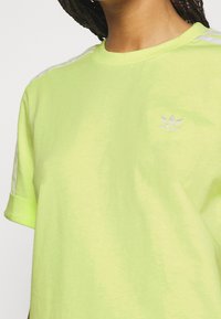 Ljusgrön bomulls t-shirt med rund halsringning, korta ärmar och vita tre-stripes detaljer på axlarna. Har en liten vit logotyp.