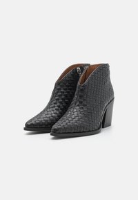 Botas de tobillo de cuero trenzado en negro con punta afilada y un tacón bloque de altura media. Cierre con cremallera en el lateral, con un forro interior suave.