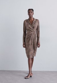 Leopardenmuster Wickelkleid in Braun und Beige, mit langen Ärmeln, einem Kragen und einer taillierten Bindung. Glatter Stoff mit einem drapierten Design.