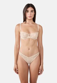 Set di lingerie in pizzo nudo con ricami floreali, reggiseno con portarimando e spalline regolabili, e perizoma abbinato con delicati dettagli.