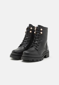 Botas de cuero negras hasta el tobillo con puntera redonda, diseño de cordones, detalles en hardware de tono dorado y suela de plataforma resistente para tracción y estabilidad.
