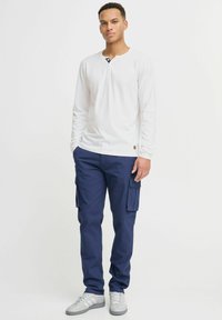 Hvit langermet henley-skjorte med marineblå krage, kombinert med marineblå cargo-bukser med sidelommer og grå joggesko.