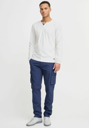 Hvid langærmet henley-shirt med en marineblå krave, parret med marineblå cargo-bukser med sidelommer og grå sneakers.