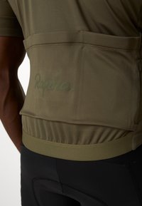 Maillot de cyclisme olive en tissu texturé, avec une poche arrière et un logo subtil "Rapha.". Maintenu en place par un ourlet élastique pour un ajustement parfait.