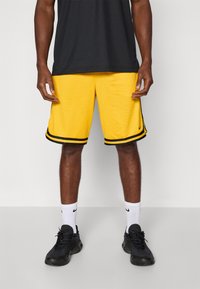 Gule basketballshorts med sorte sidestropper, tekstureret stof og en løs pasform. Båret med sorte sneakers og hvide sokker.