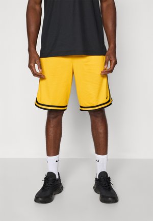 Gula basketshorts med svarta sidostreck, strukturerad tyg och lös passform. Bärs med svarta sneakers och vita strumpor.