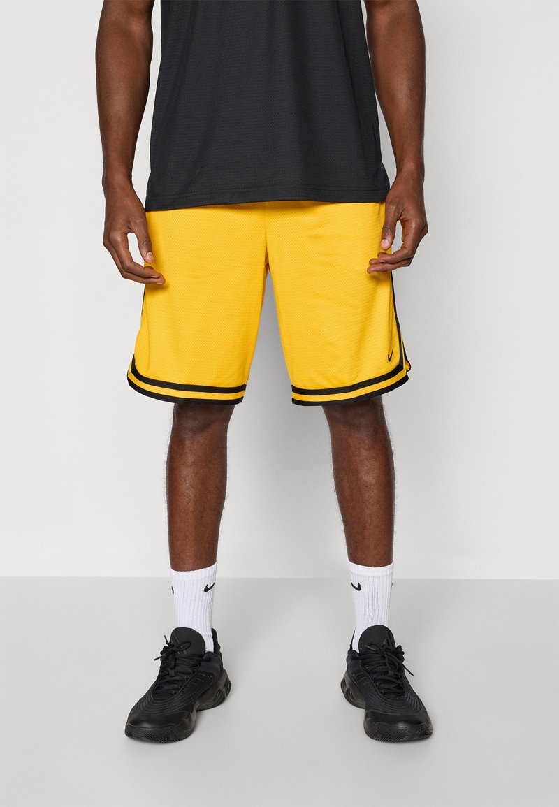 Gule basketballshorts med sorte sidestropper, tekstureret stof og en løs pasform. Båret med sorte sneakers og hvide sokker.