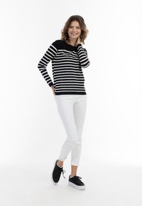 Schwarz-weiß gestreifter Pullover, lange Ärmel, Rundhalsausschnitt; kombiniert mit weißen, schmalen Hosen und schwarzen Sneakers mit dicker weißer Sohle.