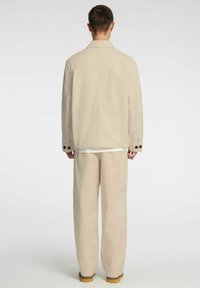 Beżowa kurtka i spodnie z gładkiego materiału; kurtka ma kołnierz i guziki na rękawach, luźny krój i prosty fason.