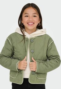 Grön vadderad jacka med huva, med tre knappar, framfickor och kontrasterande kant; bärs över en ljus hoodie.