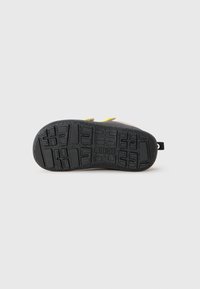 Semelle de chaussure en caoutchouc noir avec un motif texturé, mettant en avant un bord marron clair et un accent jaune au talon.