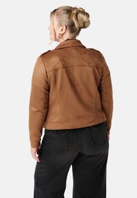 Bruine faux suède jas met een getailleerde pasvorm, schouderepauletten en een cropped lengte, gecombineerd met hoge zwarte jeans.